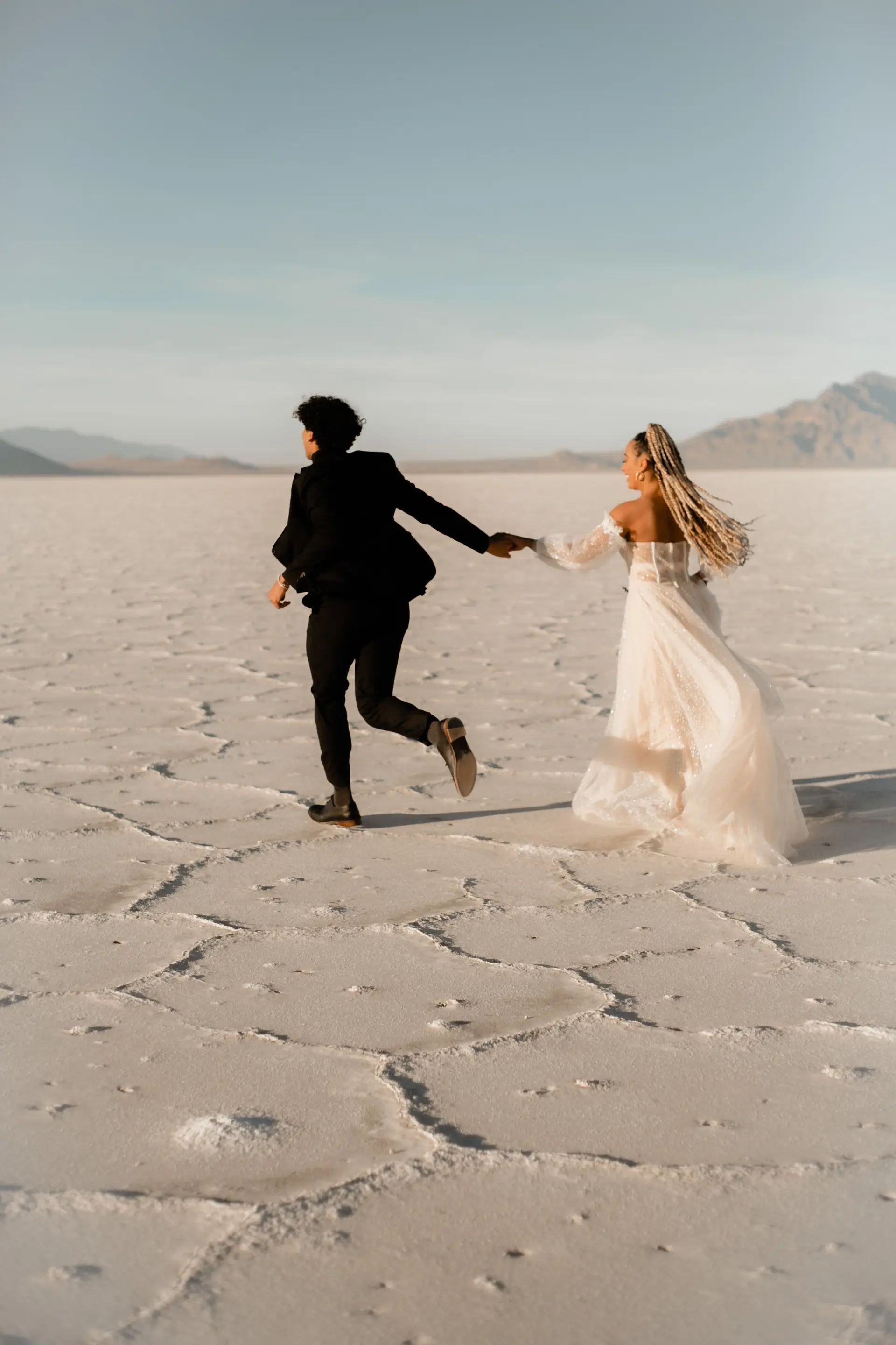 Couple holding hands and running away for their bridals at the utah salt flats