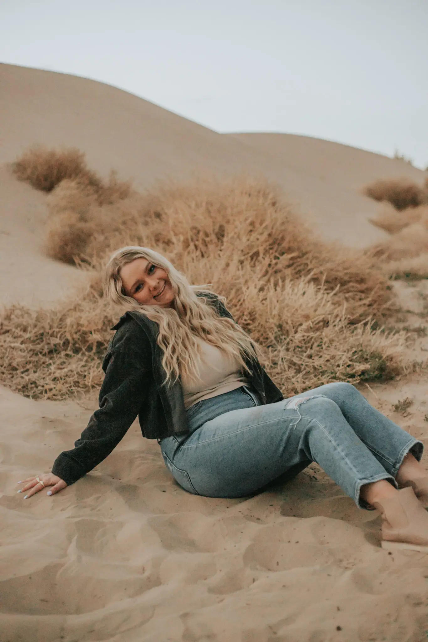 Brynelle sitting on the ground at the sand dunes and smiling