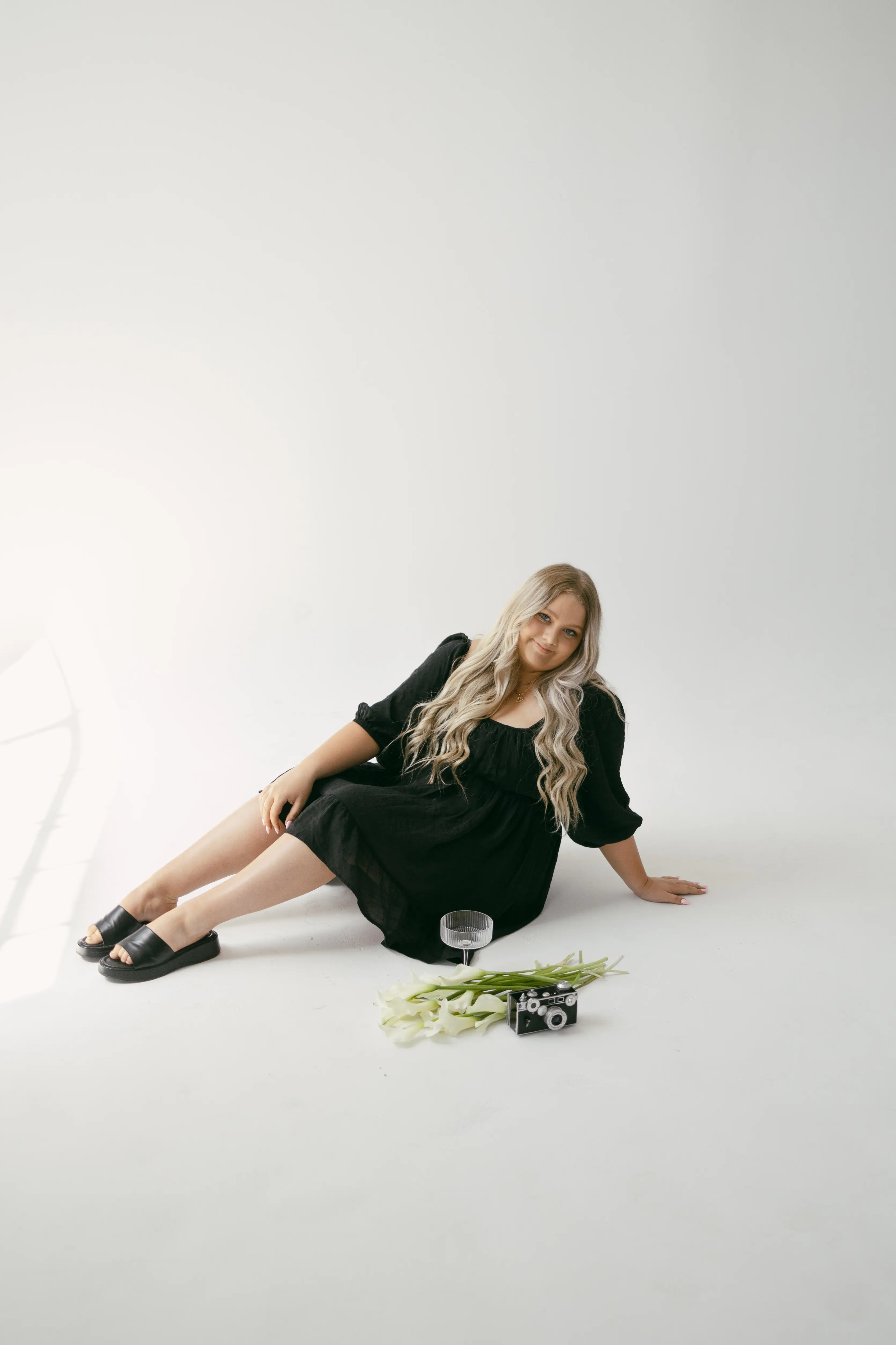 Brynelle sitting on ground, posing with a camera, glass of water, and some leaves