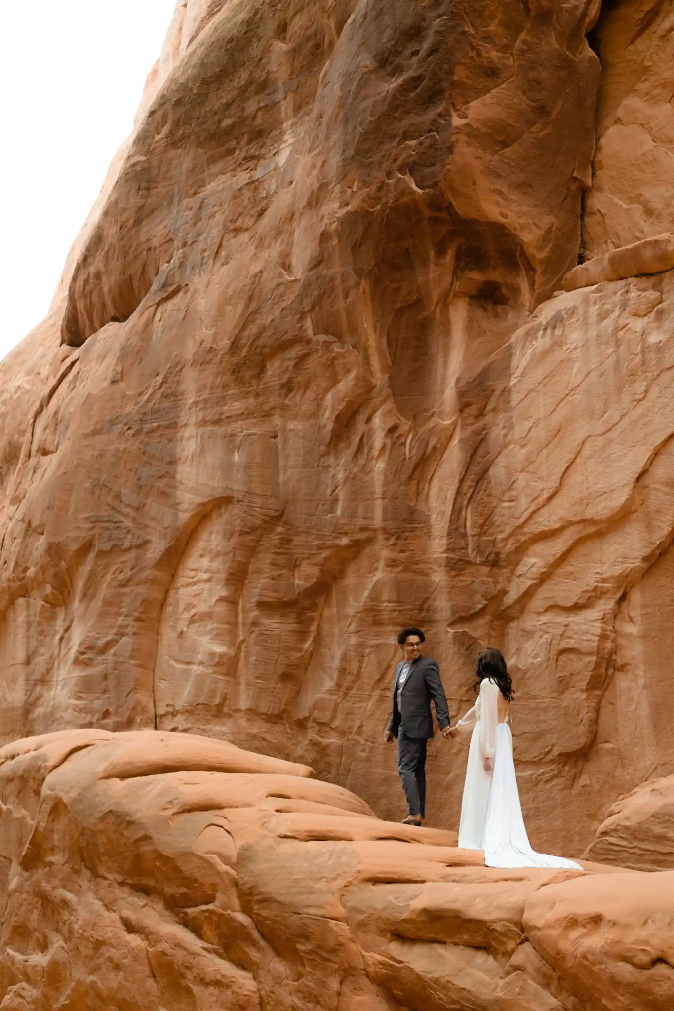 Groom leading bride up red rocks
