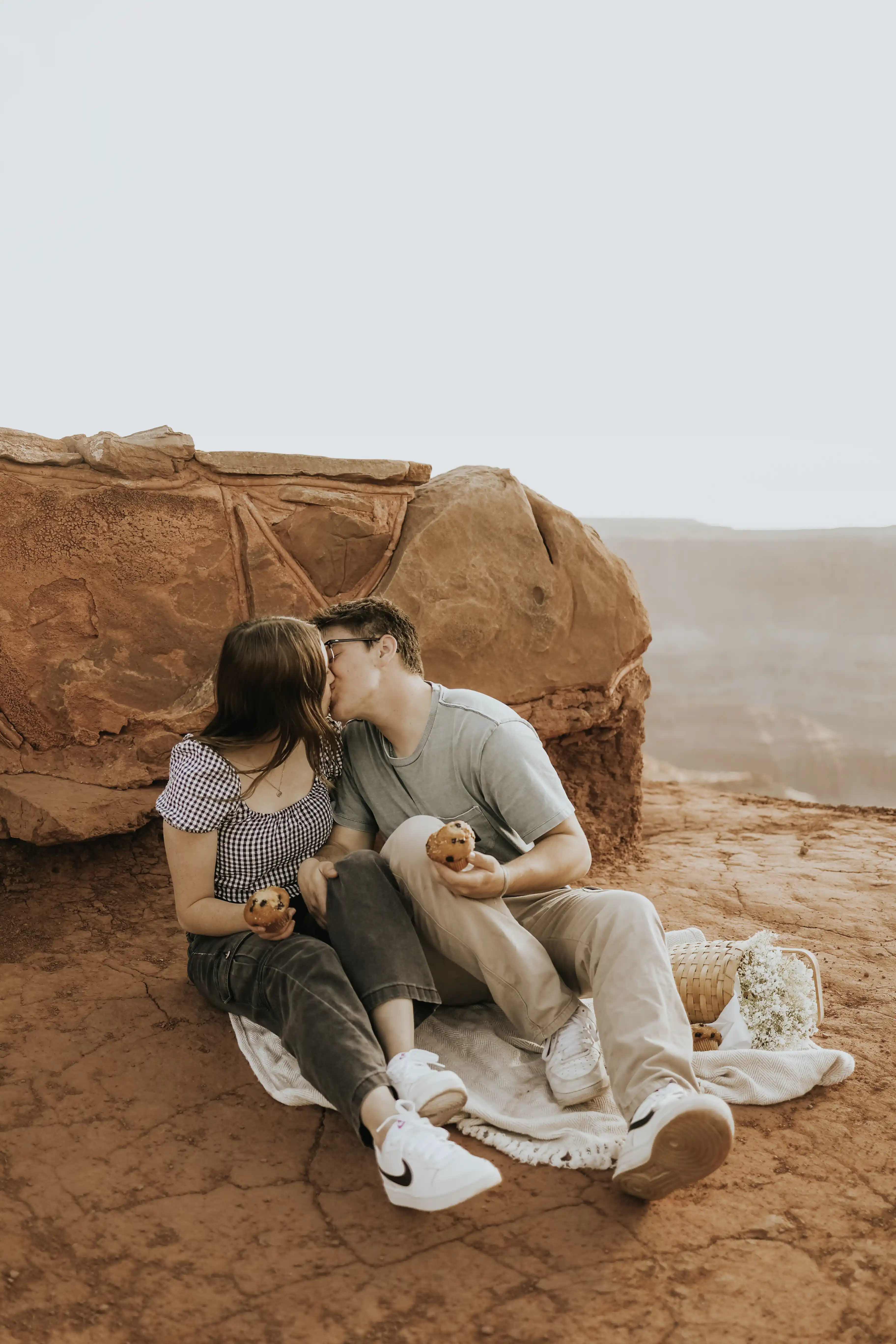 Couple sitting on blanket kissing while holding muffins