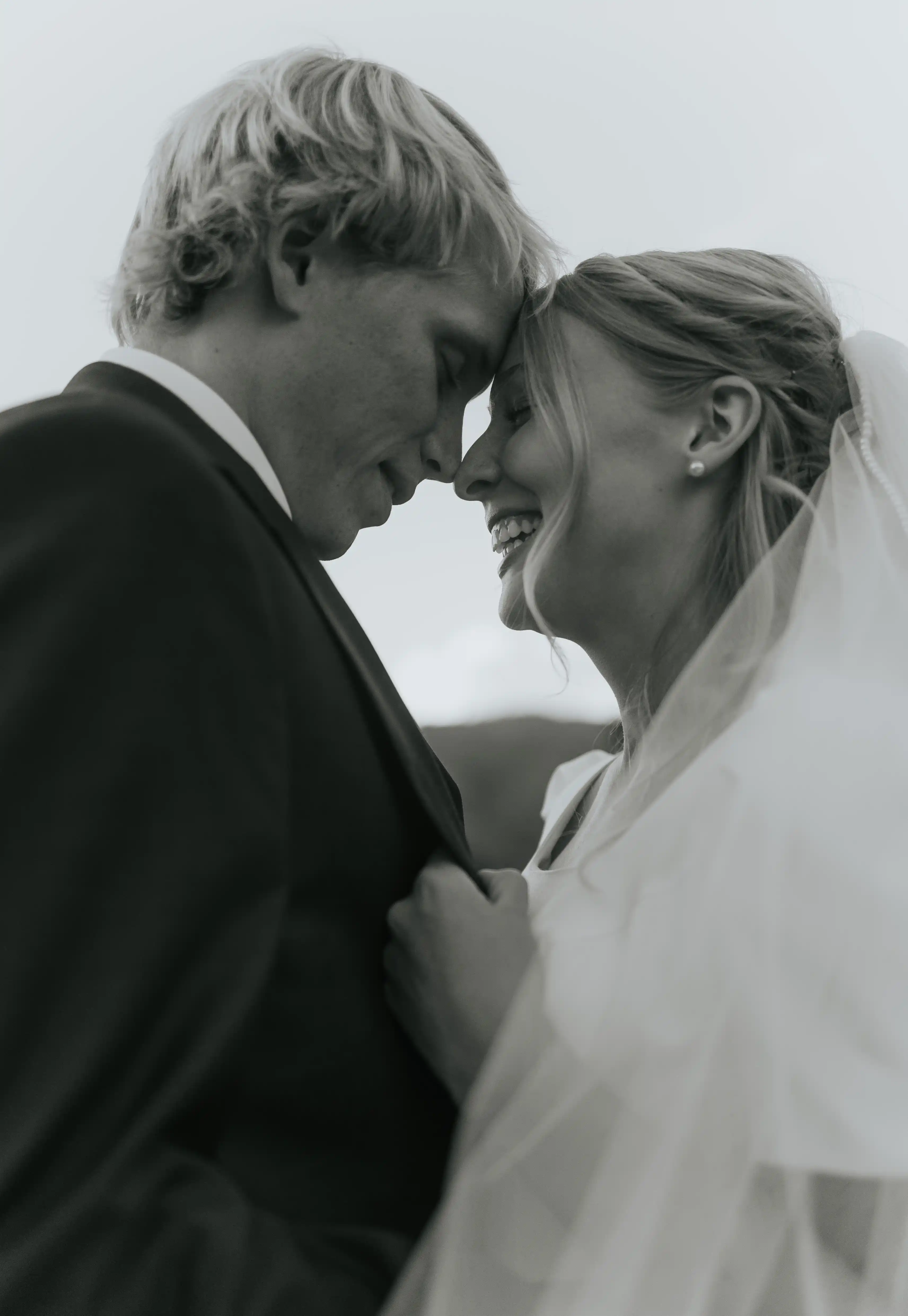 Bride holding groom in close with his jacket, nose to nose close up