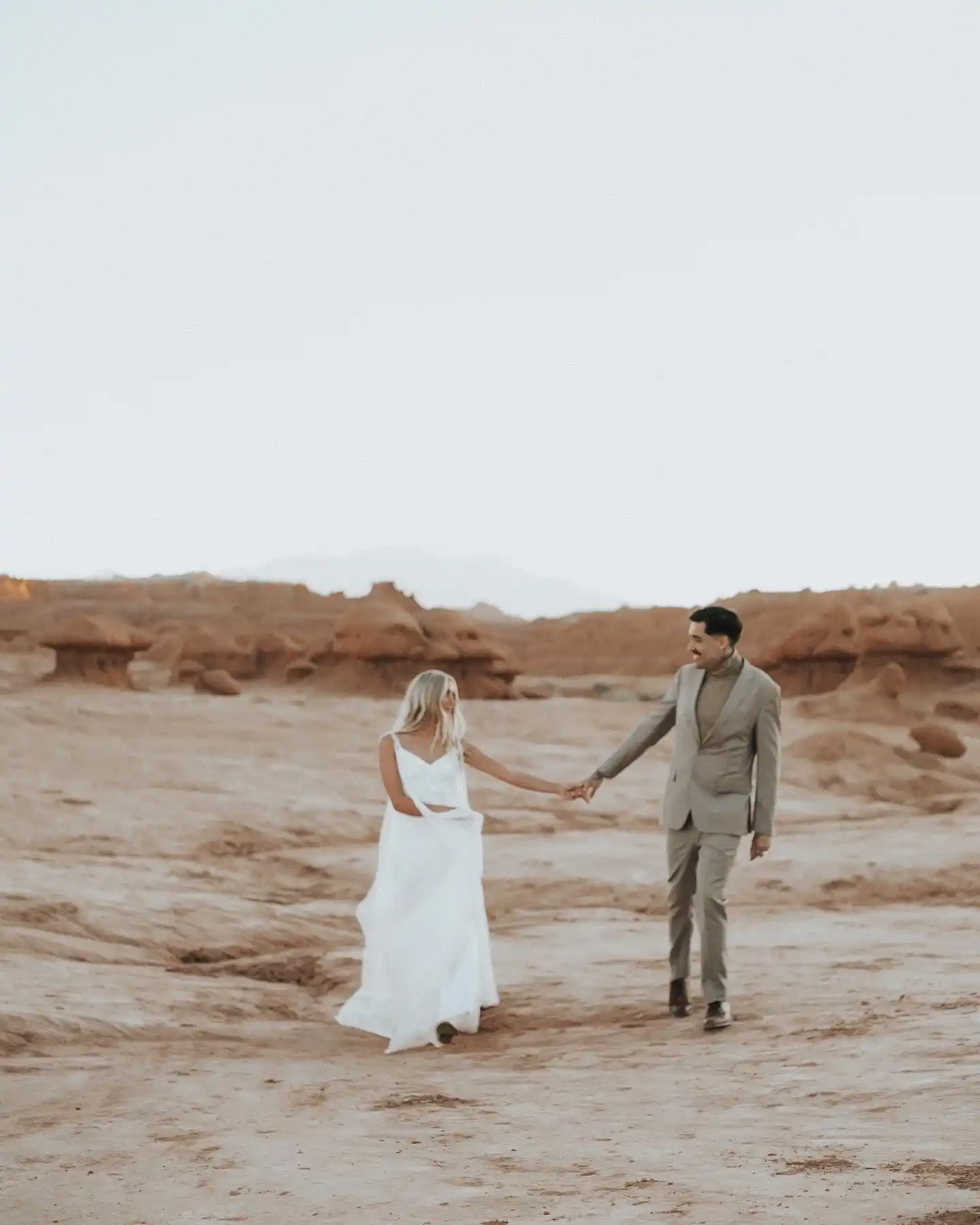 Bride and groom walking in the desert holding hands far apart