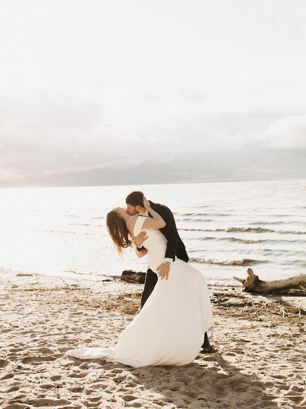 Bride sitting on rock with groom standing and looking in the distance
